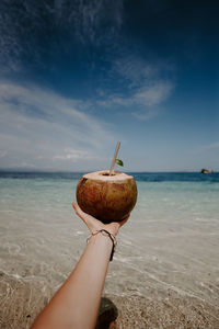 Cropped hand of woman sitting at beach against sky