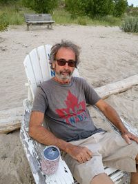 Man wearing sunglasses while sitting on chair with drinking can at beach