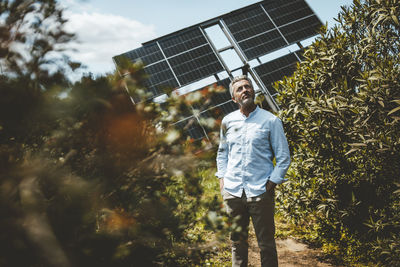 Mature man standing amidst plants in front of solar panels