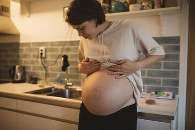 Pregnant woman showing belly in kitchen