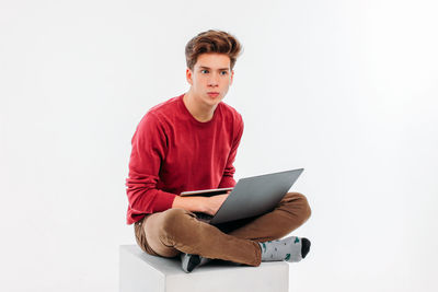 Full length of young man sitting on white background