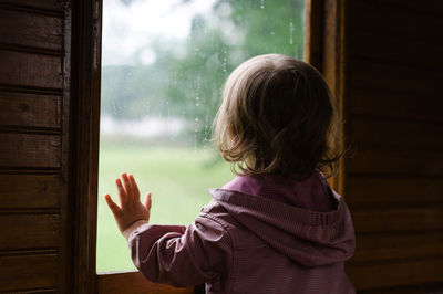 Rear view of girl looking through window at home