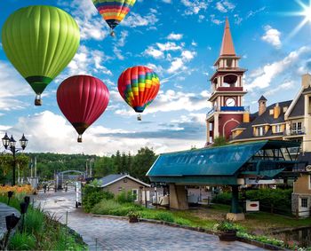 Hot air balloons flying by clock tower against blue sky