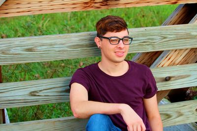 Smiling young man sitting fence 