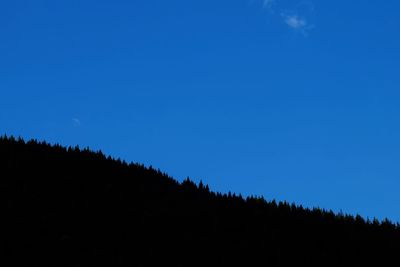 Low angle view of silhouette trees against clear blue sky