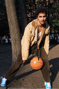 Portrait of young man standing by tree trunk