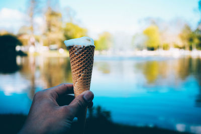 Cropped hand holding ice cream cone by lake