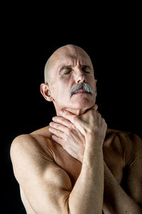 Close-up of shirtless senior man holding his neck against black background