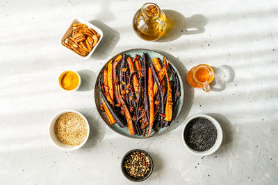 Roasted glazed spicy violet and orange carrots with ingredients on grey background. top view