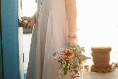 Midsection of woman holding flower bouquet while opening doorknob