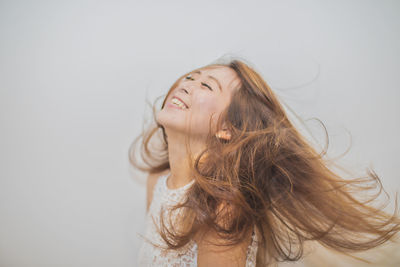 Cheerful young woman with tousled long brown hair against white background