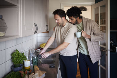 Gay couple washing dishes and drinking coffee at home