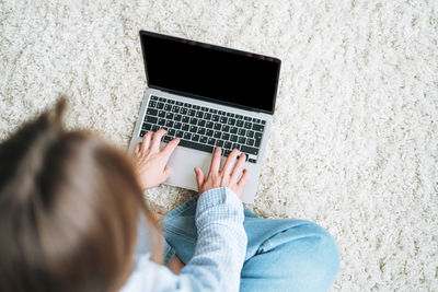 Crop photo of young woman working on laptop sitting on carpet at home, view from top