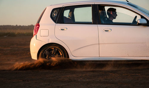 White car drifting on a reddish dirt road at sunrise time