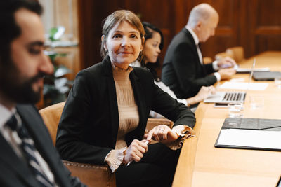 Portrait of smiling female lawyer in board room with colleagues during meeting