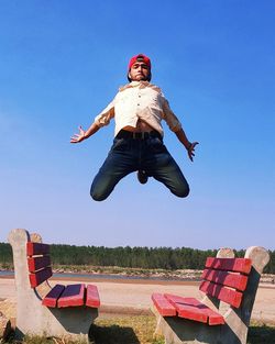 Low angle portrait of man jumping against clear blue sky