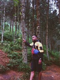 Portrait of young man standing against trees in forest