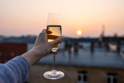 Girl holding a glass of champagne into the sunset.