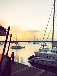 Silhouette sailboats moored at harbor against sky during sunset