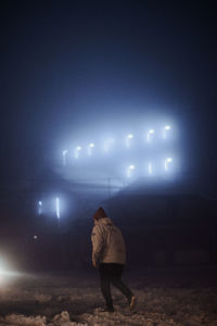 Rear view of man walking on illuminated street at night