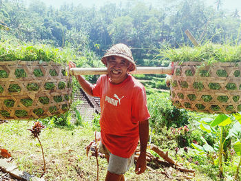 Full length portrait of smiling man standing against plants