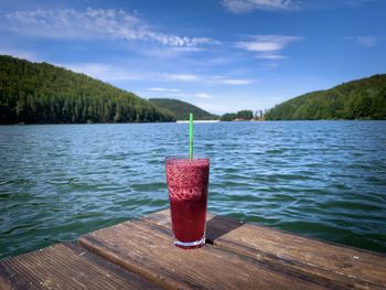 Glass with strawberry lemonade placed on a wooden pontoon near the lake on a bright summer day