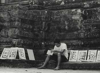 Full length of man sitting on book against building