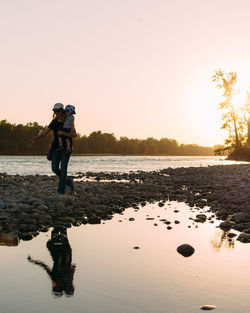 People standing on shore against sky during sunset