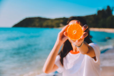 Young woman holding orange fruit at beach