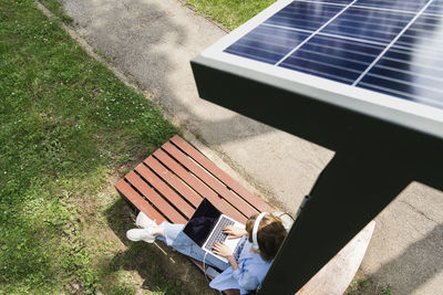 Woman using laptop sitting under solar charging point at park