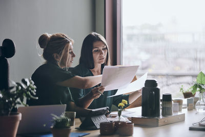 Confident female entrepreneurs discussing over documents during meeting in board room at office