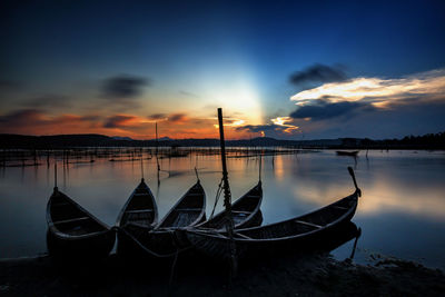 Boat moored in lake against sky during sunset