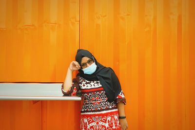 Portrait of woman wearing mask standing against orange wall