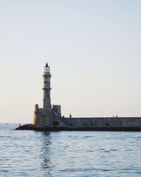 Lighthouse by sea against clear sky