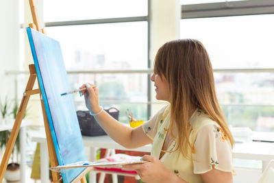 Side view of woman holding book against window