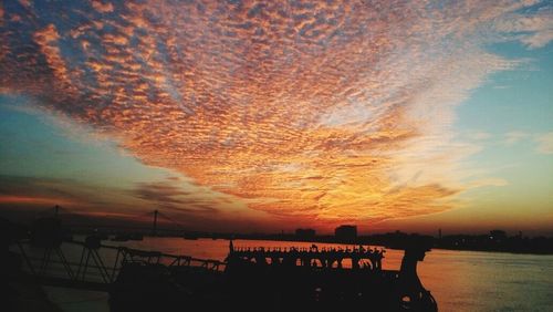 Silhouette boats in sea against dramatic sky during sunset