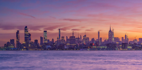 Illuminated modern buildings in city against sky during sunset