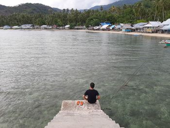 Rear view of man sitting on riverbank