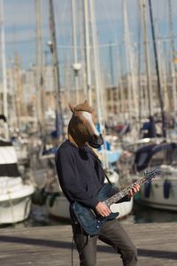 Man wearing horse mask while playing guitar at harbor