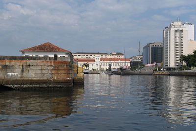 Buildings by river against sky in city