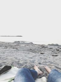 Low section of man sitting on beach against clear sky