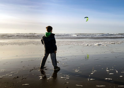 Rear view of boy looking at kite flying over sea