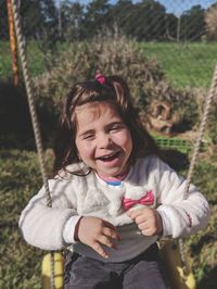 Portrait of happy girl on swing during sunny day