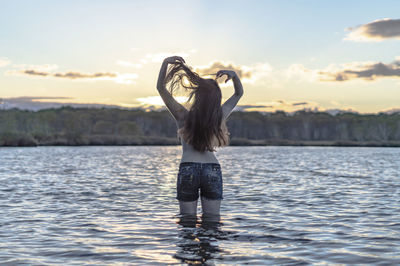 Rear view of shirtless woman standing in lake against sky