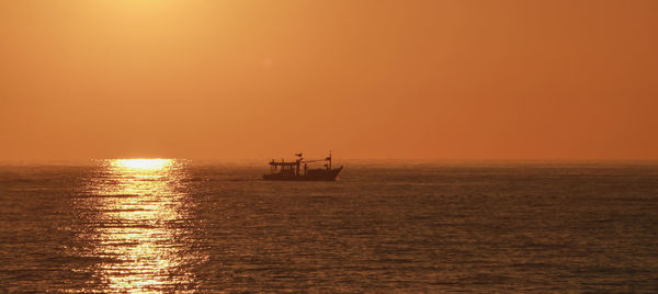 Silhouette boat in sea against orange sky