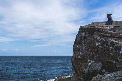 Low angle view of man standing on cliff by sea against sky