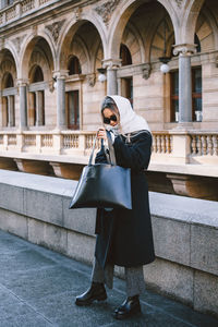 Woman wearing sunglasses standing against built structure