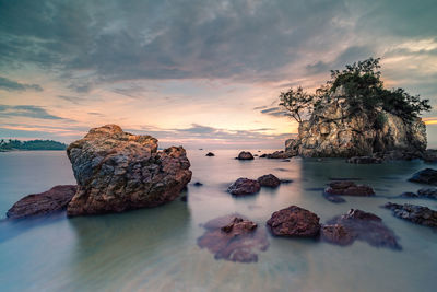 Rocks in sea against sky during sunset