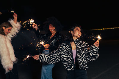 Smiling women holding sparkler enjoying outdoors at night