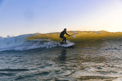 Man surfing in sea against sky during sunset